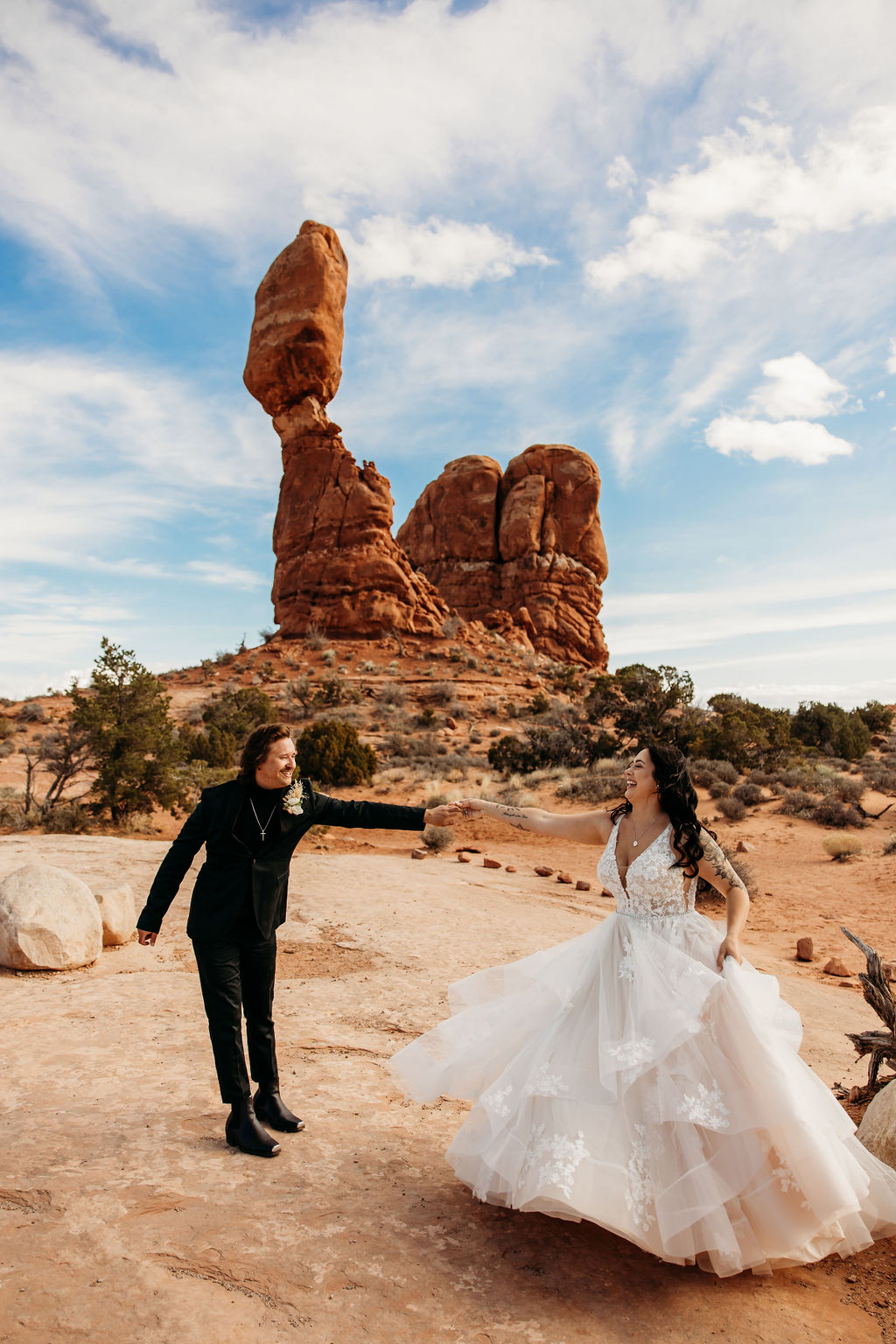 A couple holds hands while walking near a towering rock formation under a clear sky.