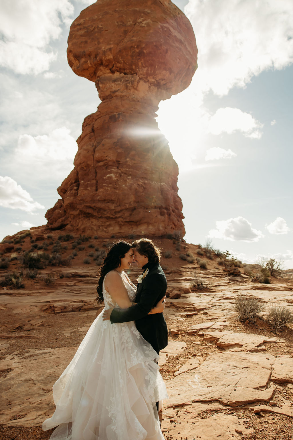 A couple in wedding attire embracing in front of the balanced rock formation. 
