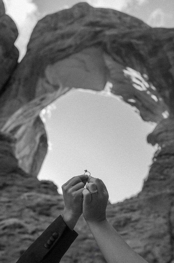 Two hands holding a ring aligned with a natural rock arch in the background.