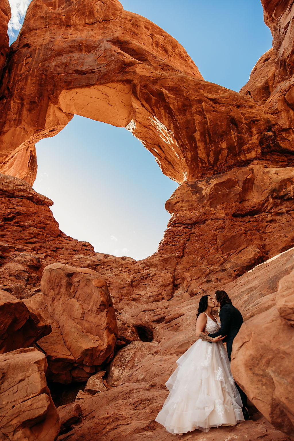 Couple in wedding attire sharing a moment under a natural sandstone arch at Arches National Park | PHOTOGRAPHY BY BROGAN |  5 REASONS TO HAVE A MOAB NATIONAL PARK ELOPEMENT 