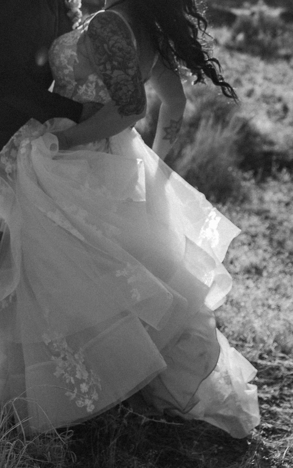 A woman in a lace-sleeved wedding dress walking in sunlight, captured in a black and white photograph at Arches National Park