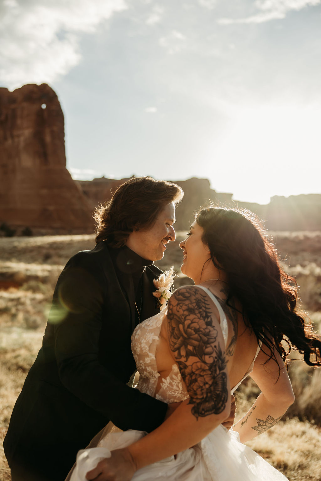 A couple in wedding attire embracing in front of the balanced rock formation in arches national park. | PHOTOGRAPHY BY BROGAN |  5 REASONS TO HAVE A MOAB NATIONAL PARK ELOPEMENT 
