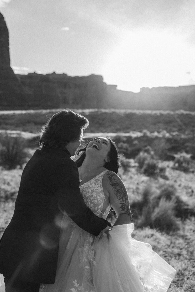 A monochrome photo of a couple in wedding attire sharing an intimate moment outdoors with natural rock formations in the background at Arches National Park