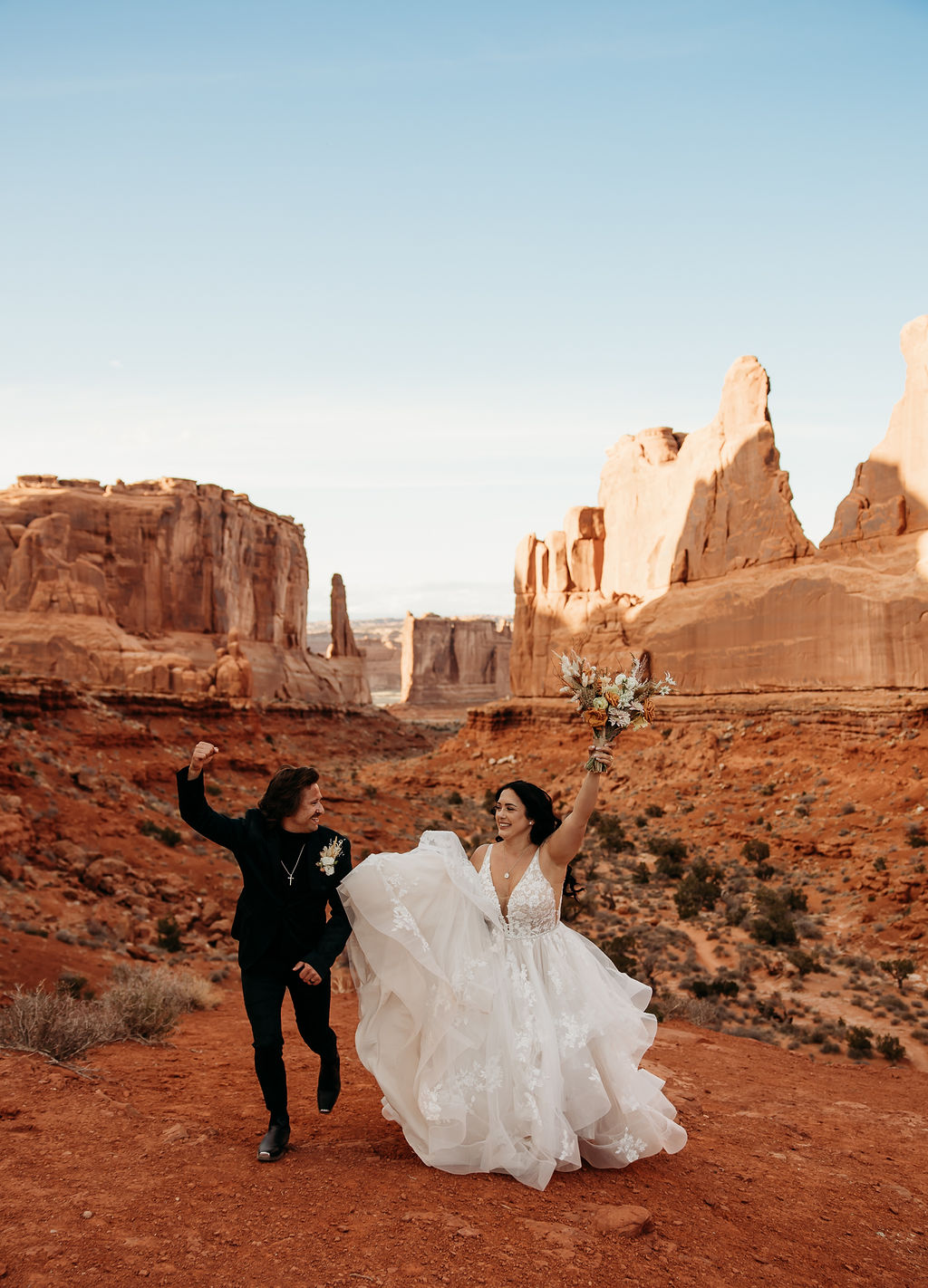 A couple in wedding attire embracing in front of the balanced rock formation. | PHOTOGRAPHY BY BROGAN |  5 REASONS TO HAVE A MOAB NATIONAL PARK ELOPEMENT 