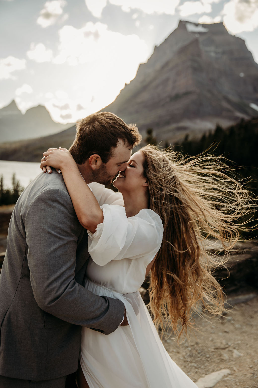 A couple embraces and kisses, surrounded by a mountainous landscape, with the woman's hair blowing in the wind taken by Montana elopement photographer