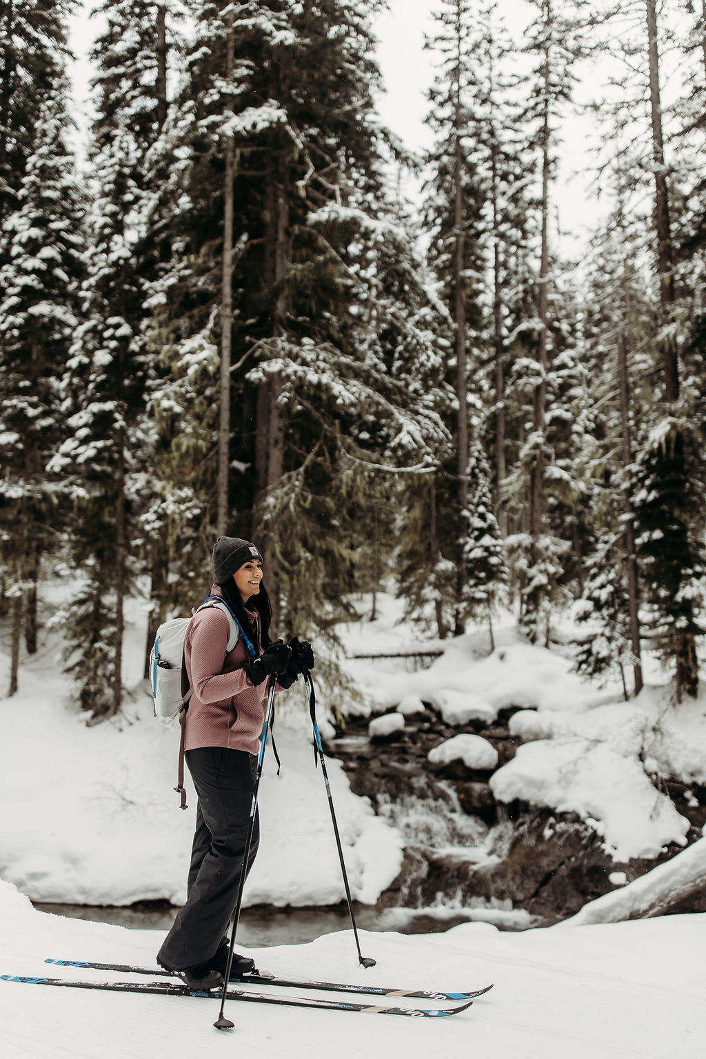 Brogan montana elopement photographer cross-country skiing in a snowy forest with a creek in the background.