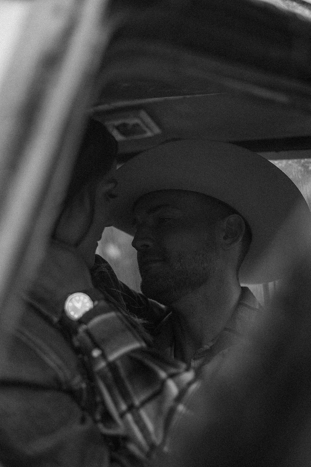 A couple sits close together inside an old, black truck parked in a forested area.