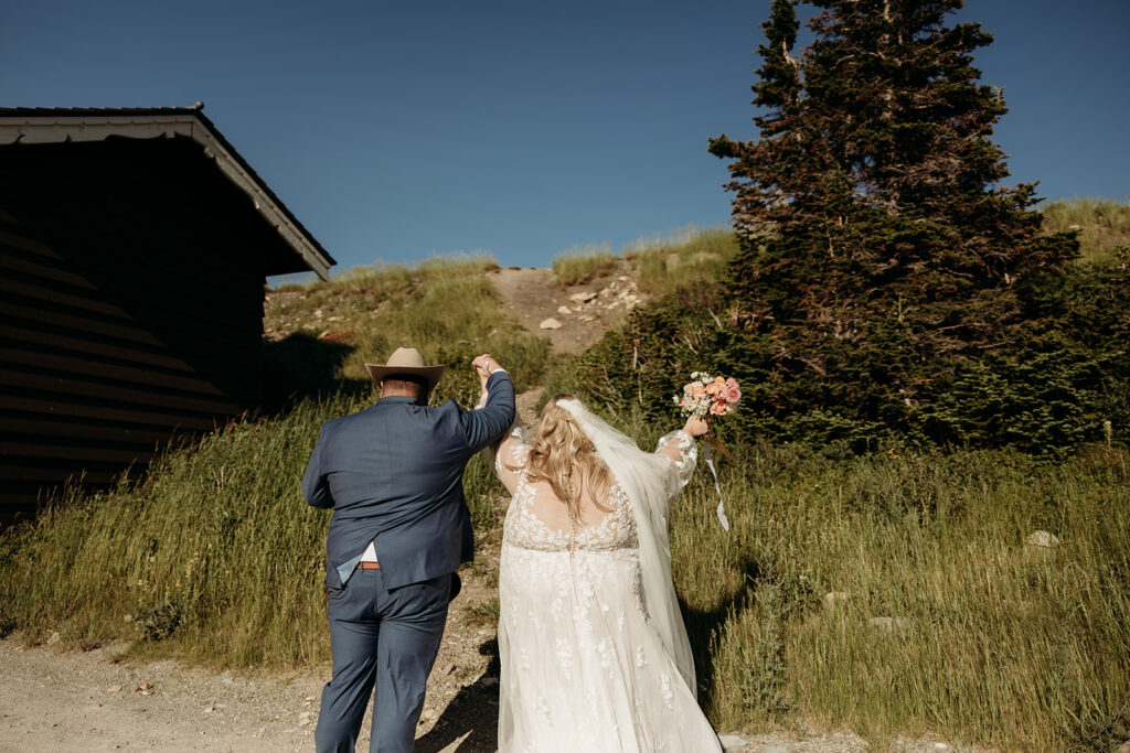 Bride and groom walking hand in hand along a mountain trail in GNP.
