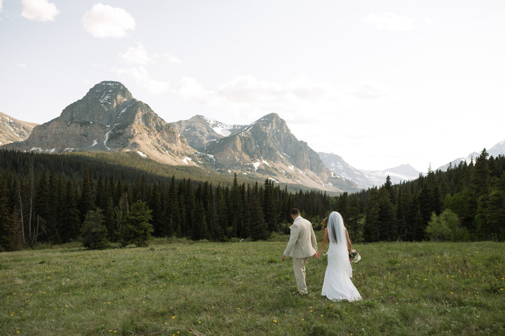 Bride and groom walking through a mountain meadow in Glacier National Park
