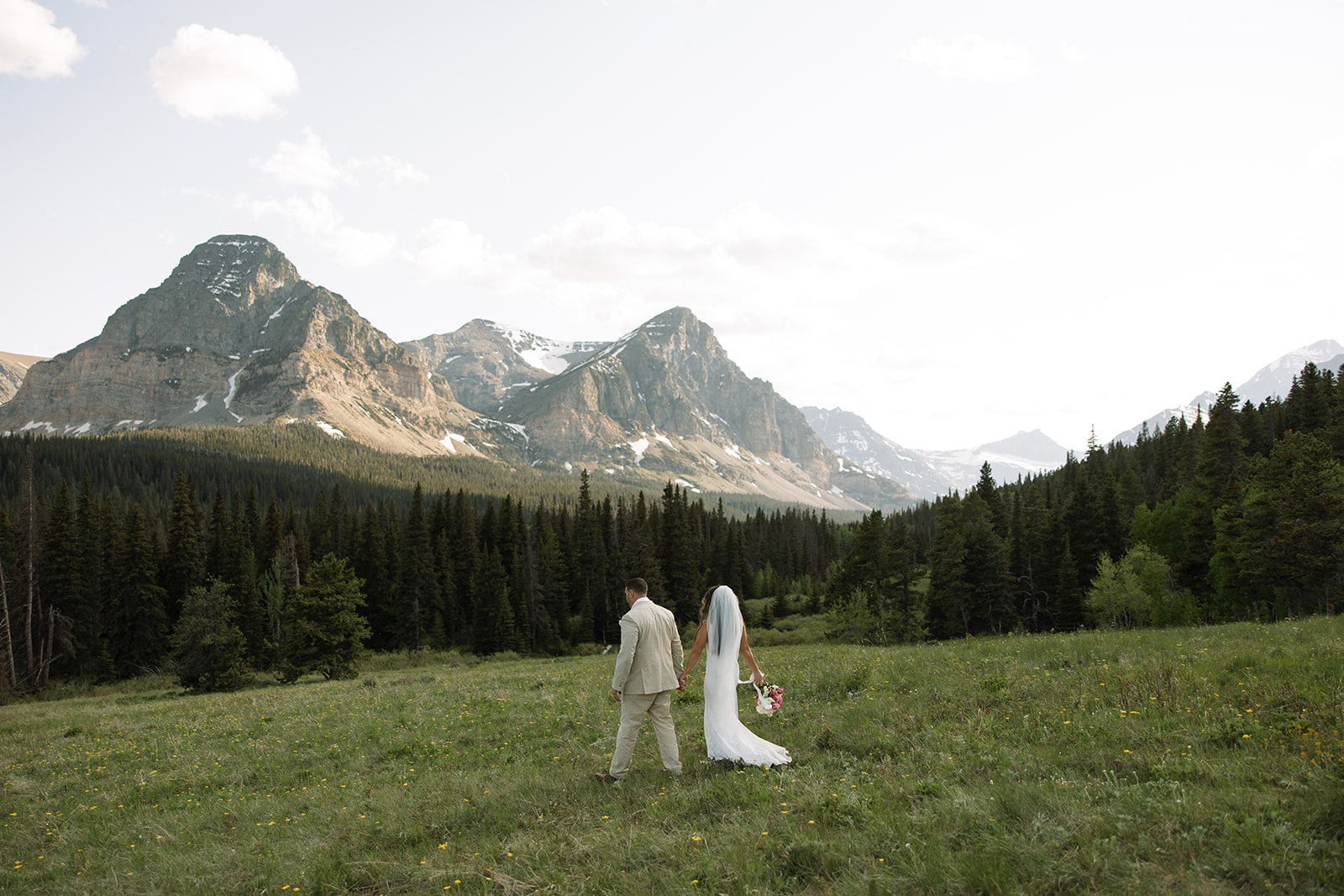Bride and groom walking through a mountain meadow in Glacier National Park