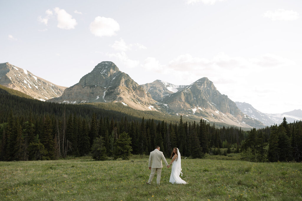 Bride and groom walking through a mountain meadow in Glacier National Park
