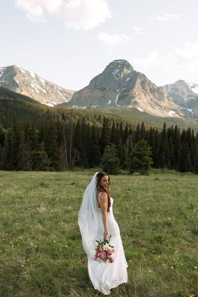 Bride holding pink bouquet and looking over her shoulder with mountains in the background

