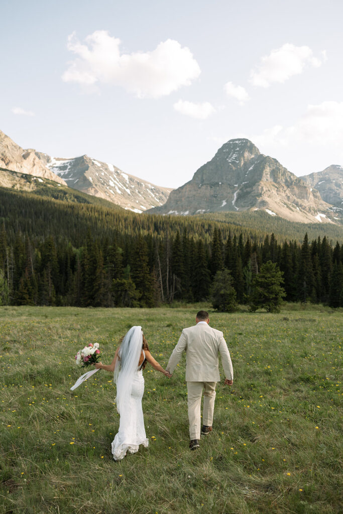 Bride and groom walking through a mountain meadow in Glacier National Park

