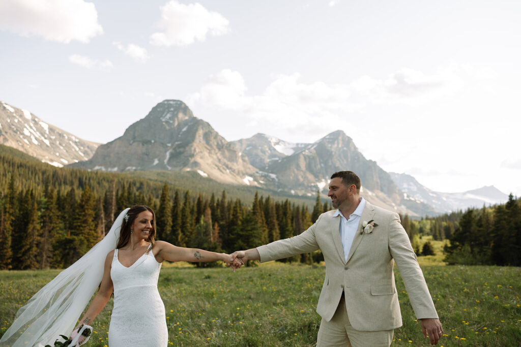 Bride and groom walking through a mountain meadow in Glacier National Park
