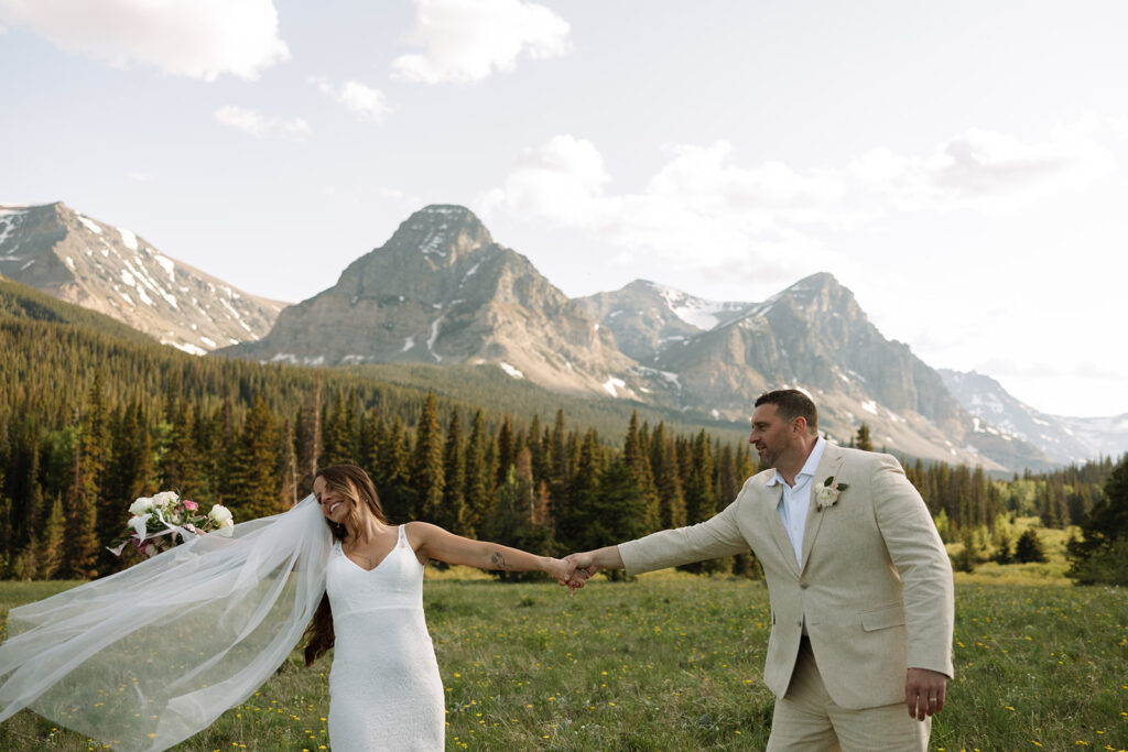 Bride and groom walking through a mountain meadow in Glacier National Park
