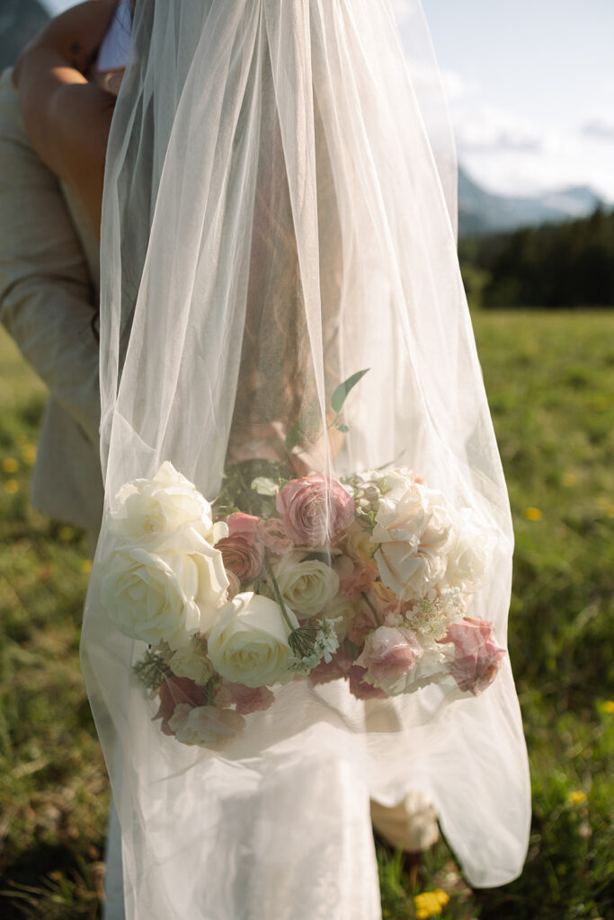 Bride holding pink bouquet and looking over her shoulder with mountains in the background
