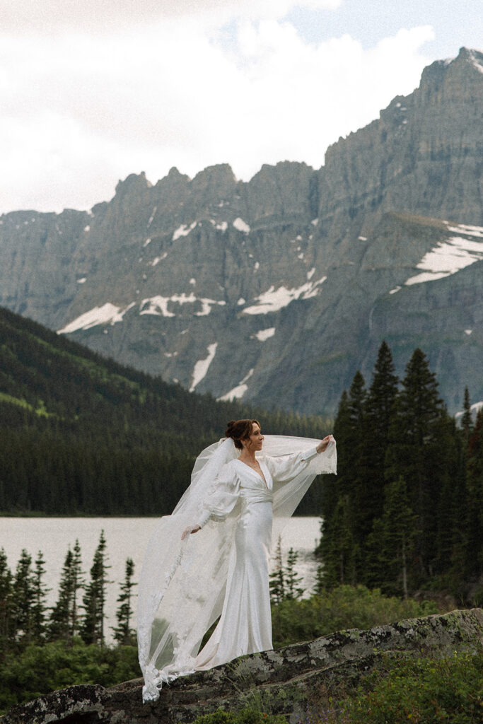 Bride and groom standing by Josephine Lake shoreline surrounded by mountains.
