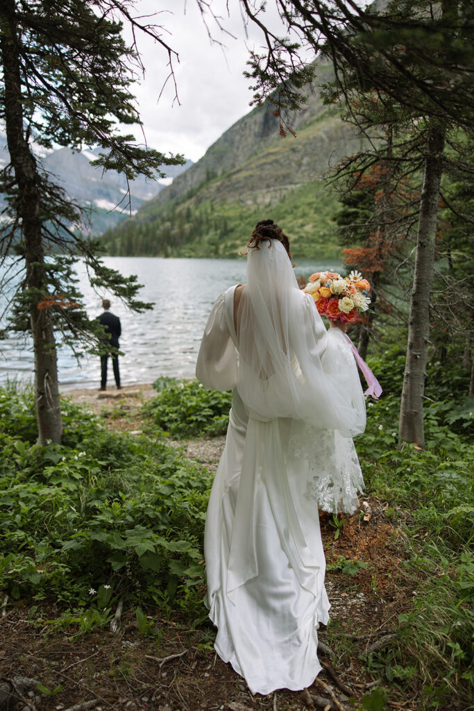 Bride and groom standing by Josephine Lake shoreline surrounded by mountains.
