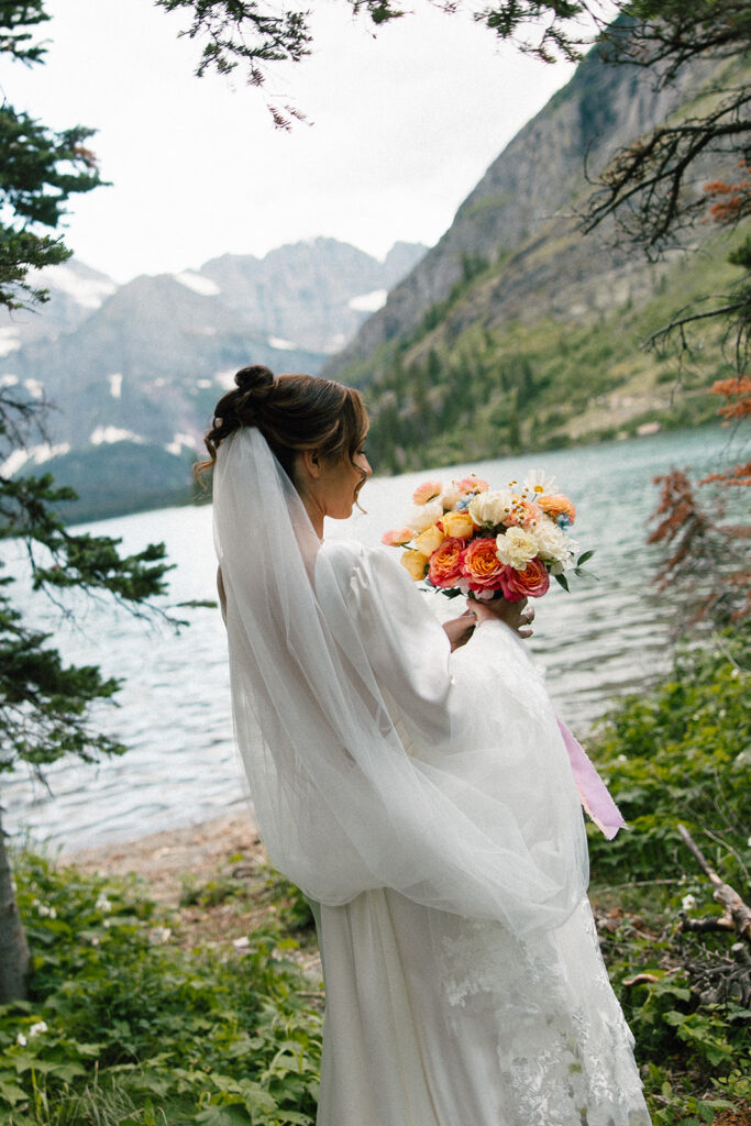 Bride and groom standing by Josephine Lake shoreline surrounded by mountains.
