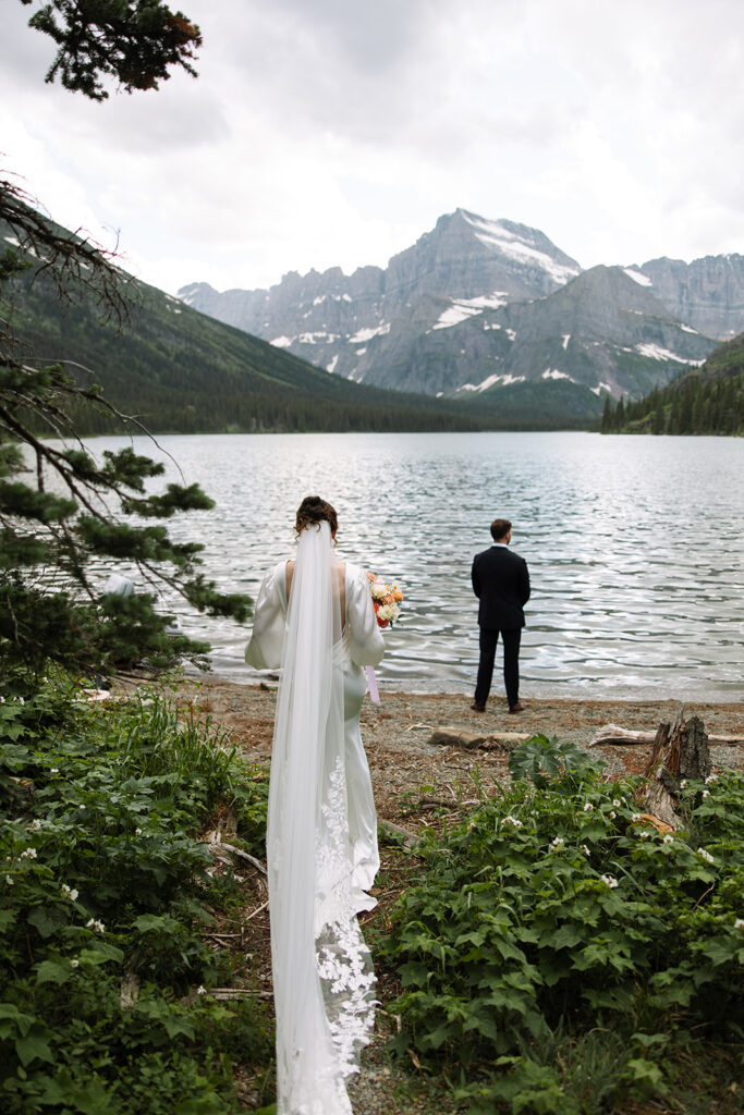 Bride and groom standing by Josephine Lake shoreline surrounded by mountains.
