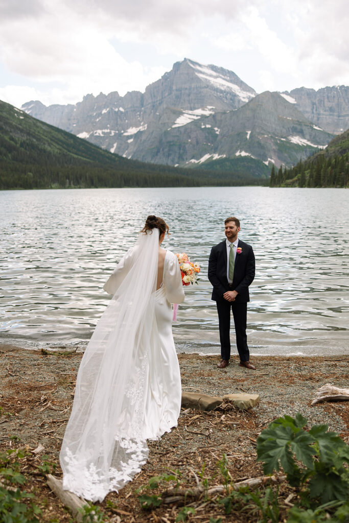 Bride and groom standing by Josephine Lake shoreline surrounded by mountains.
