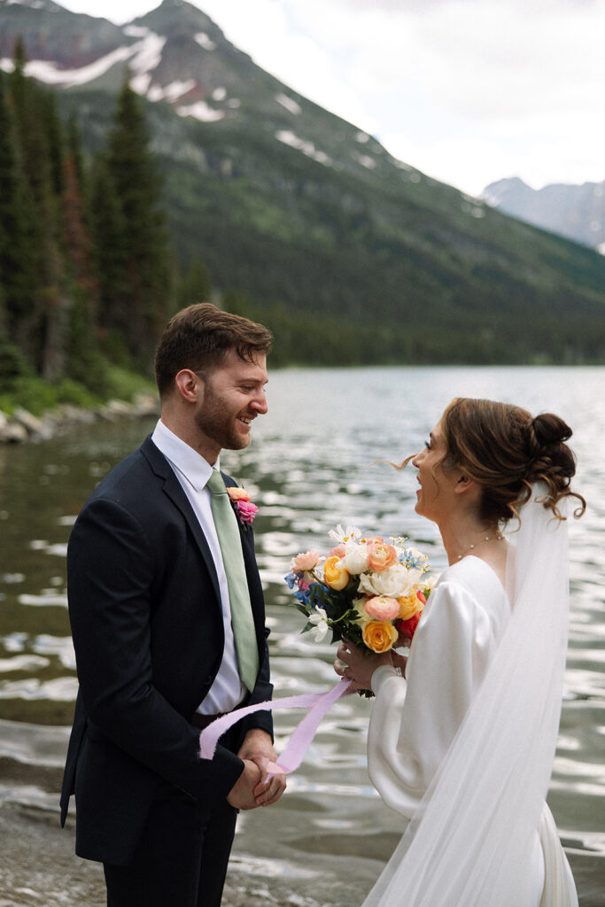 Bride and groom standing by Josephine Lake shoreline surrounded by mountains.
