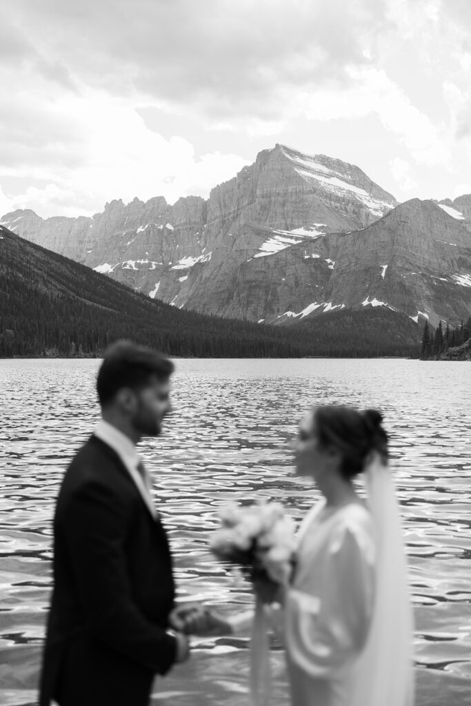 Bride and groom standing by Josephine Lake shoreline surrounded by mountains.
