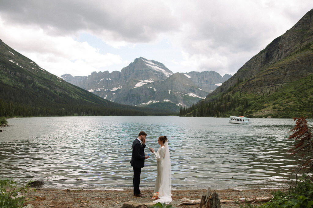 Bride and groom standing by Josephine Lake shoreline surrounded by mountains.
