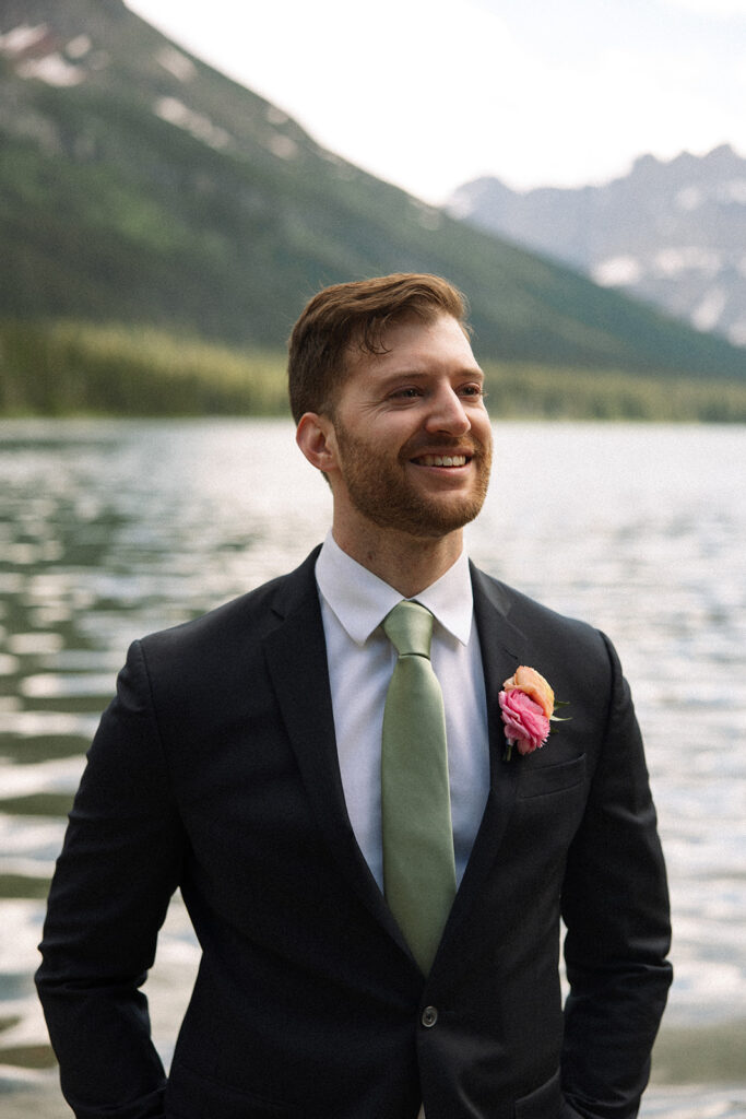 Bride and groom standing by Josephine Lake shoreline surrounded by mountains.
