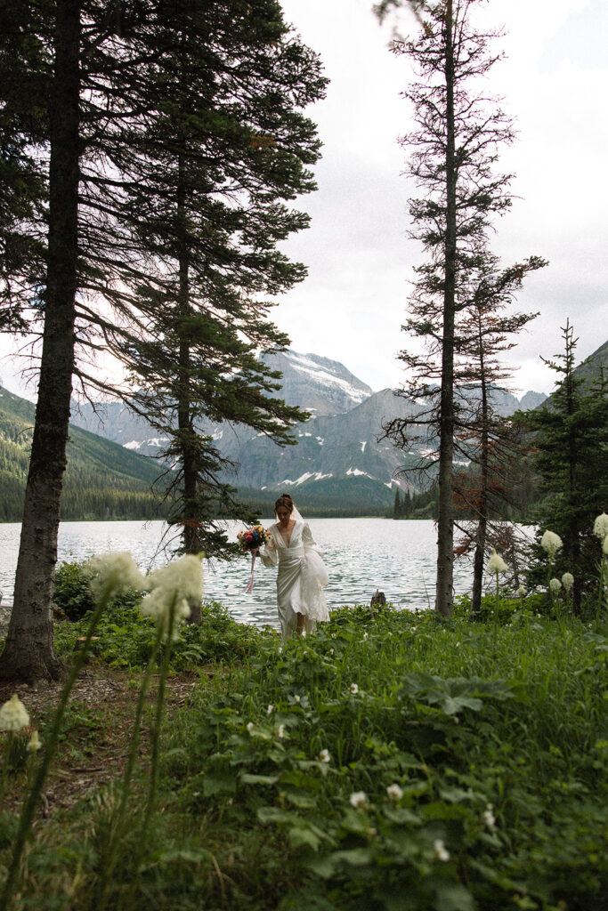 Bride and groom standing by Josephine Lake shoreline surrounded by mountains.
