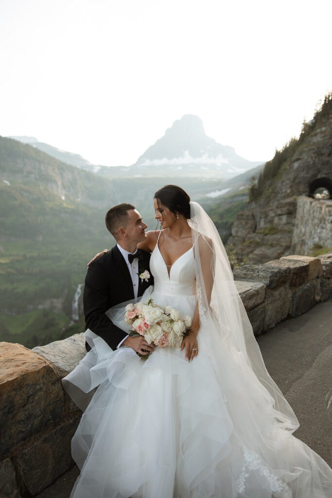 Couple standing together along Going to the Sun Road with mountains in the background
