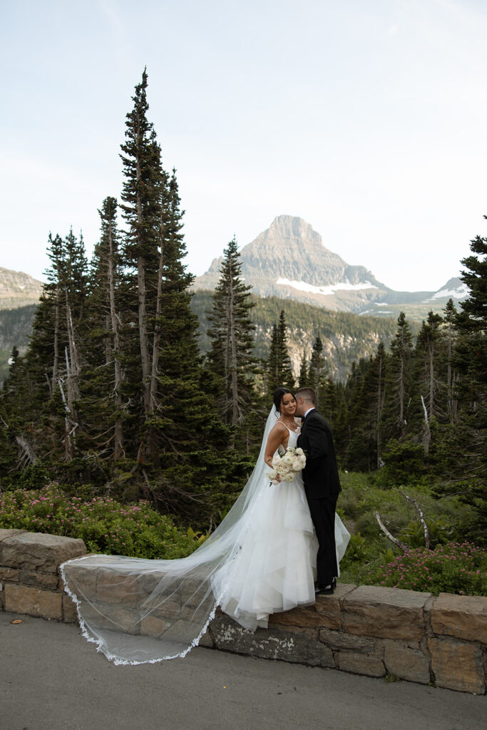 Couple standing together along Going to the Sun Road with mountains in the background
