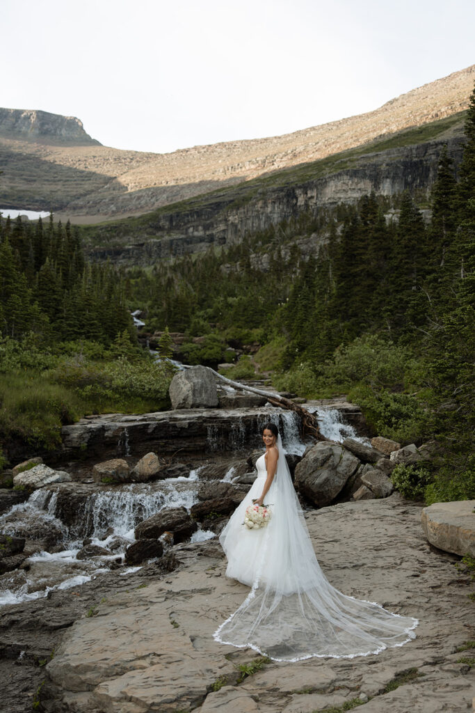 Couple standing together along Going to the Sun Road with mountains in the background
