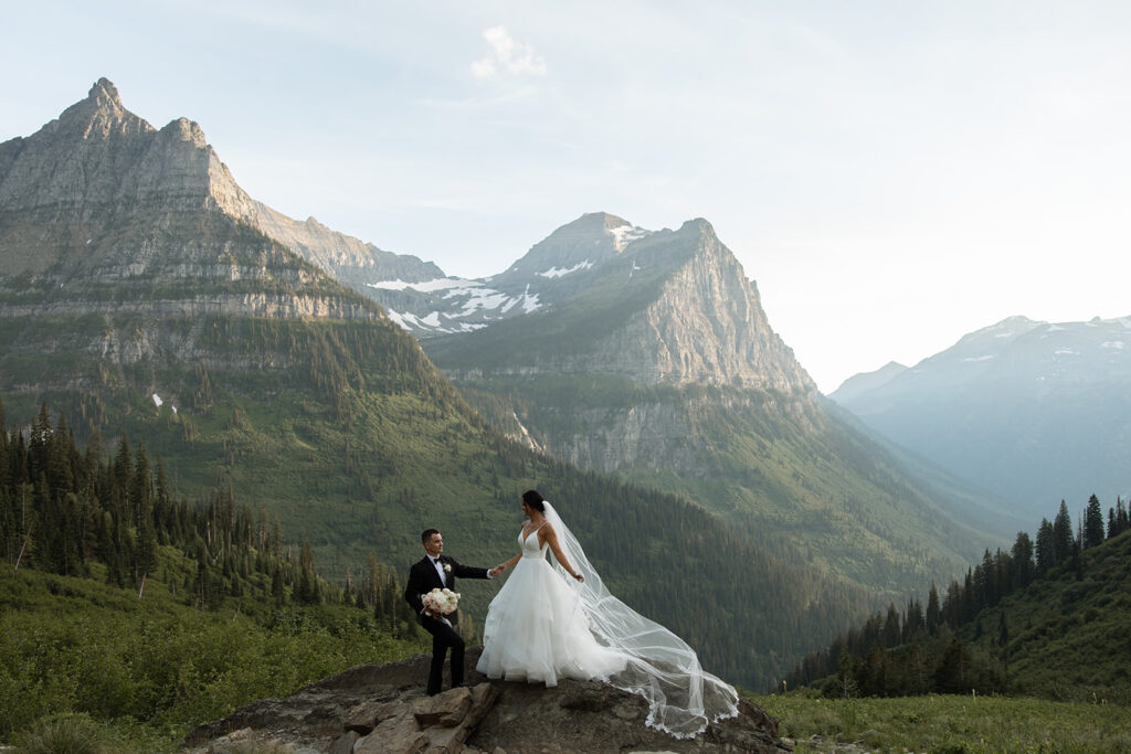 Couple standing together along Going to the Sun Road with mountains in the background
