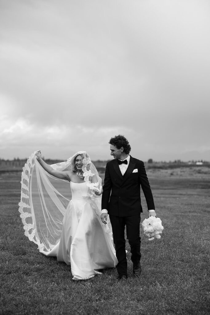 Bride and groom holding hands beside a lake with golden sunset reflections.
