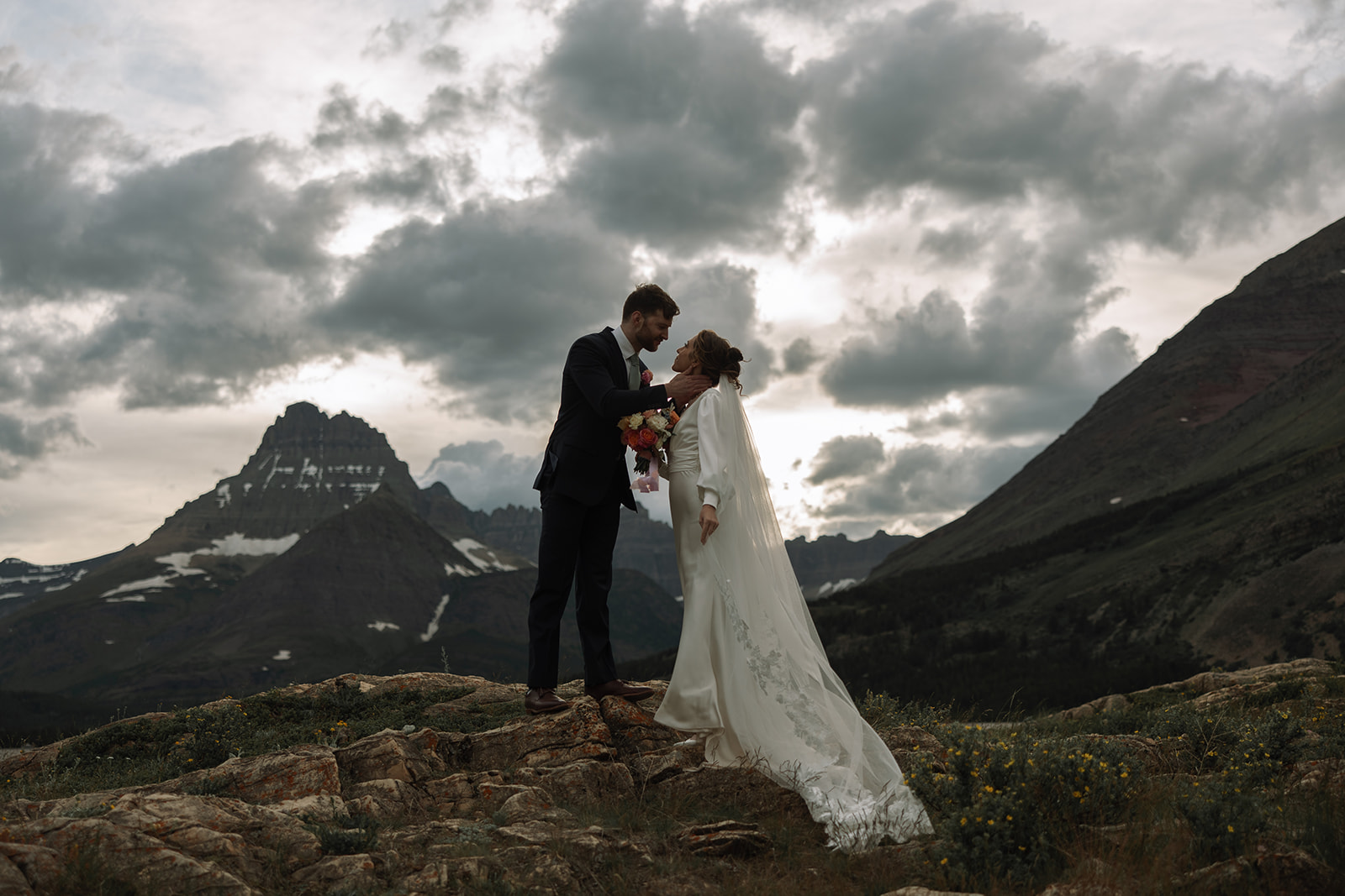 Couple sharing an intimate sunrise elopement at Many Glacier with alpenglow lighting the mountains behind them in Glacier National Park.