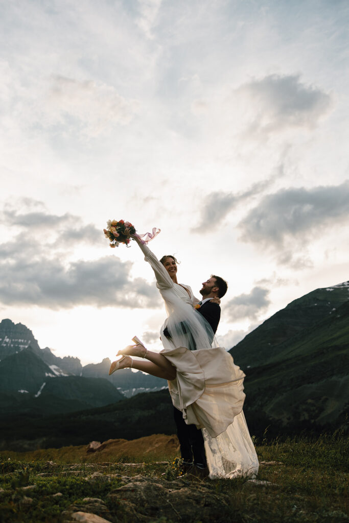 Couple sharing an intimate sunrise elopement at Many Glacier with alpenglow lighting the mountains behind them in Glacier National Park.
