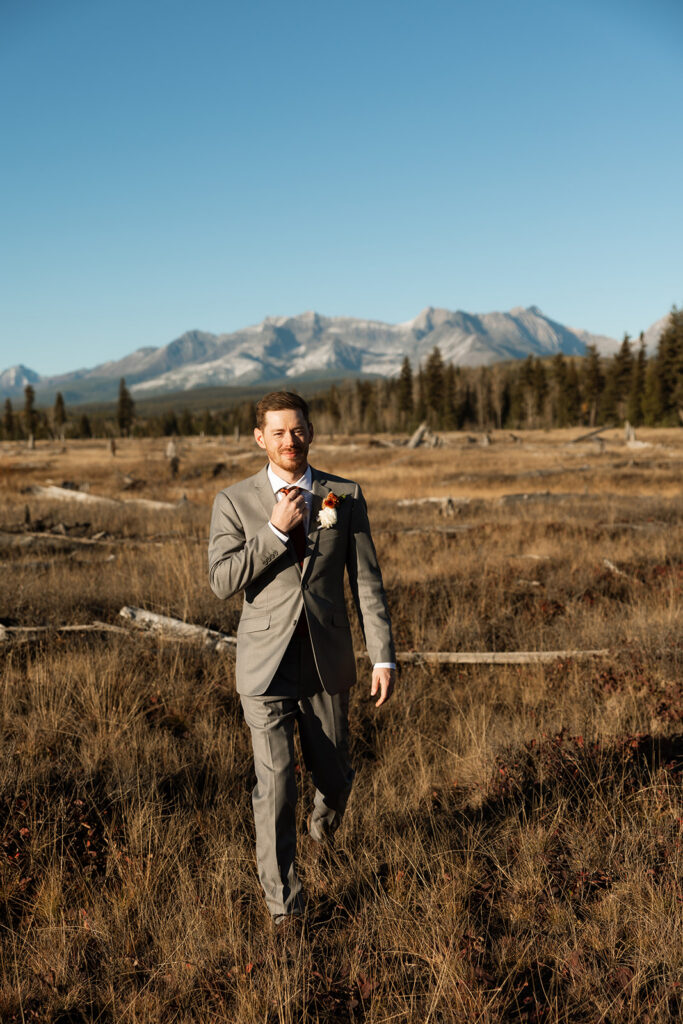 Bride and groom walking hand in hand with mountains and water in the background.