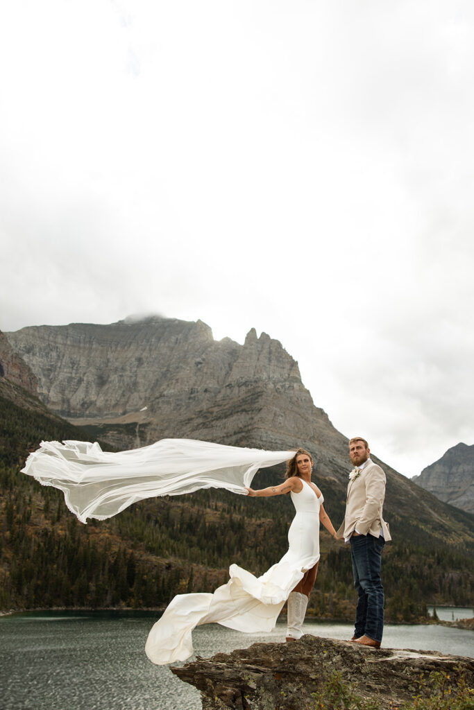 Bride and groom walking hand in hand with mountains and water in the background.