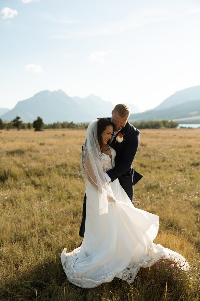 Bride and groom walking hand in hand with mountains and water in the background.