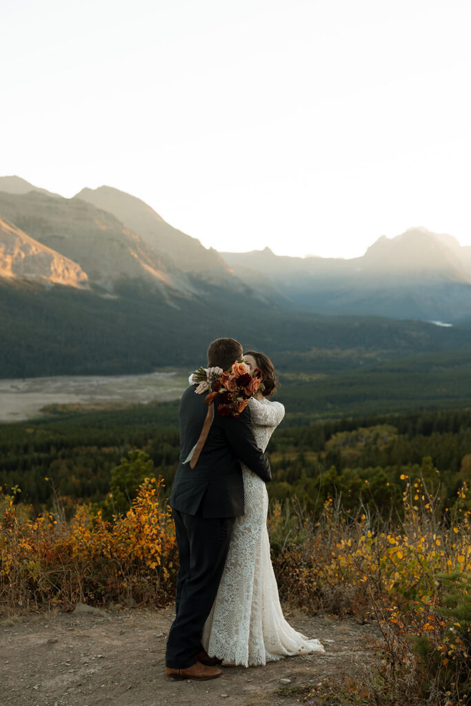 Bride and groom walking hand in hand with mountains and water in the background.