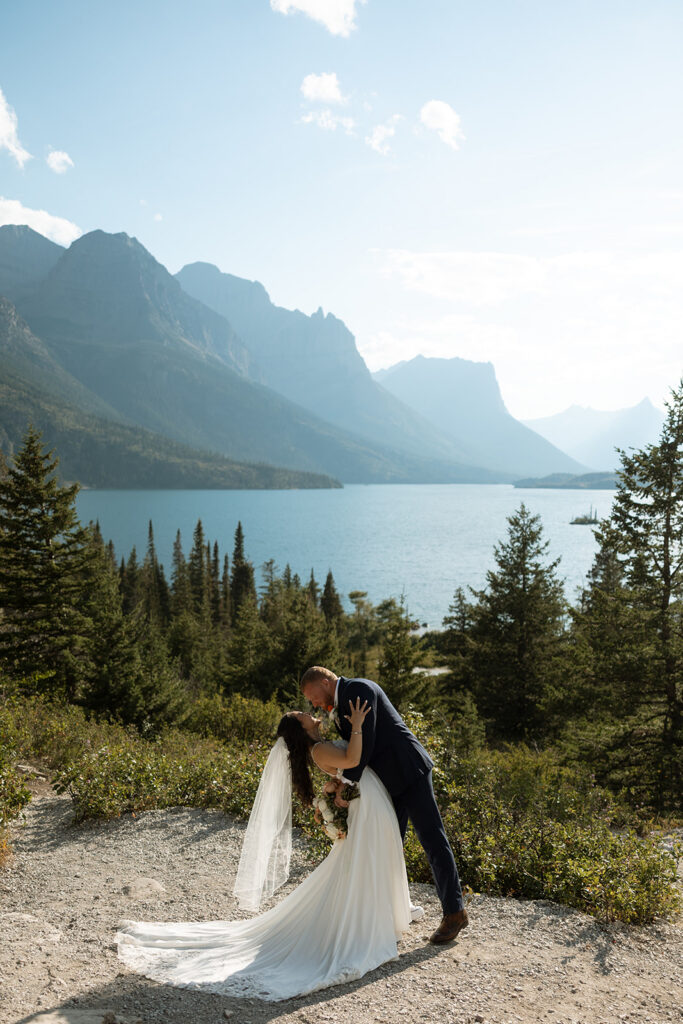 Bride and groom walking hand in hand with mountains and water in the background.