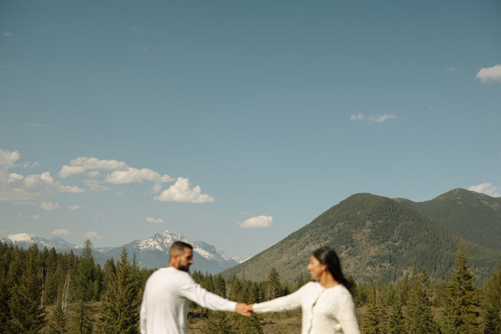 Couple holding hands in a wide open landscape during their Glacier National Park engagement session
