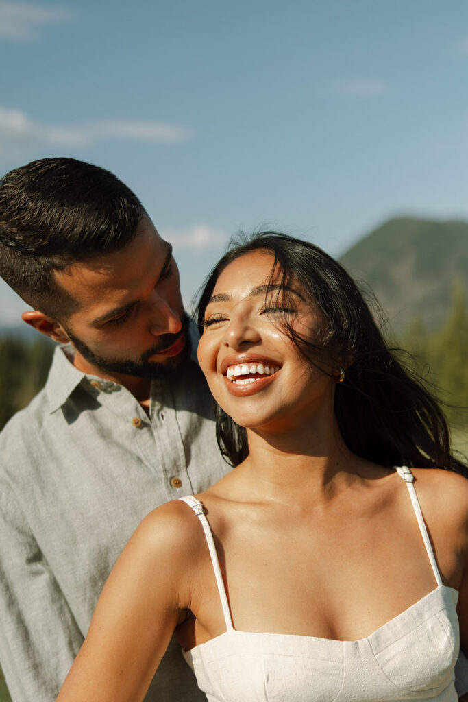 Couple embracing with mountains and fresh greenery in the background at Glacier National Park
