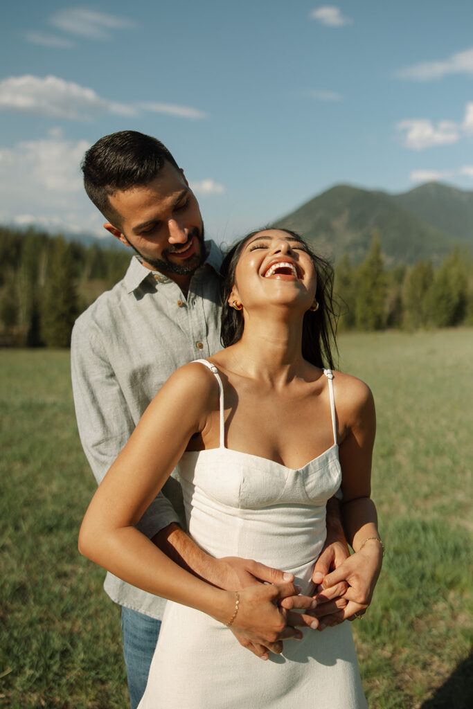 Couple embracing with mountains and fresh greenery in the background at Glacier National Park

