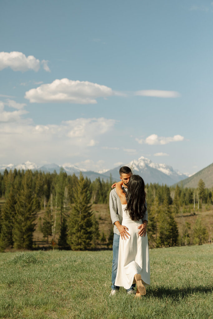 Couple embracing with mountains and fresh greenery in the background at Glacier National Park
