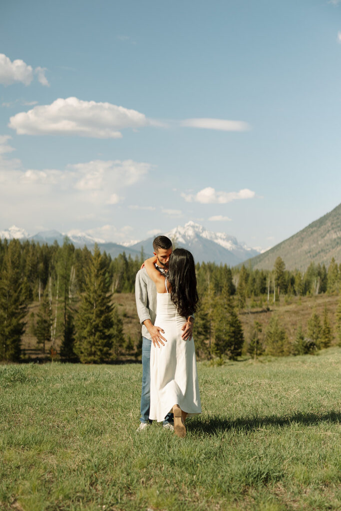 Couple embracing with mountains and fresh greenery in the background at Glacier National Park