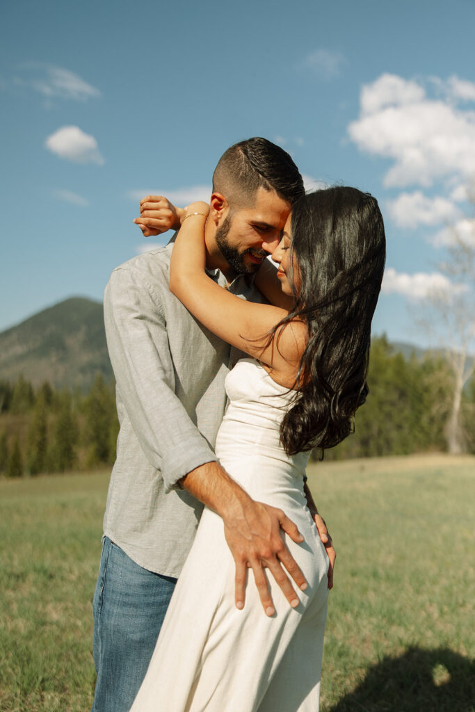 Candid engagement photo of couple exploring Glacier National Park with snowy peaks and spring landscape

