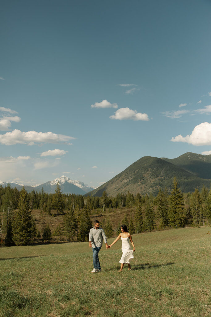 Candid engagement photo of couple exploring Glacier National Park with snowy peaks and spring landscape

