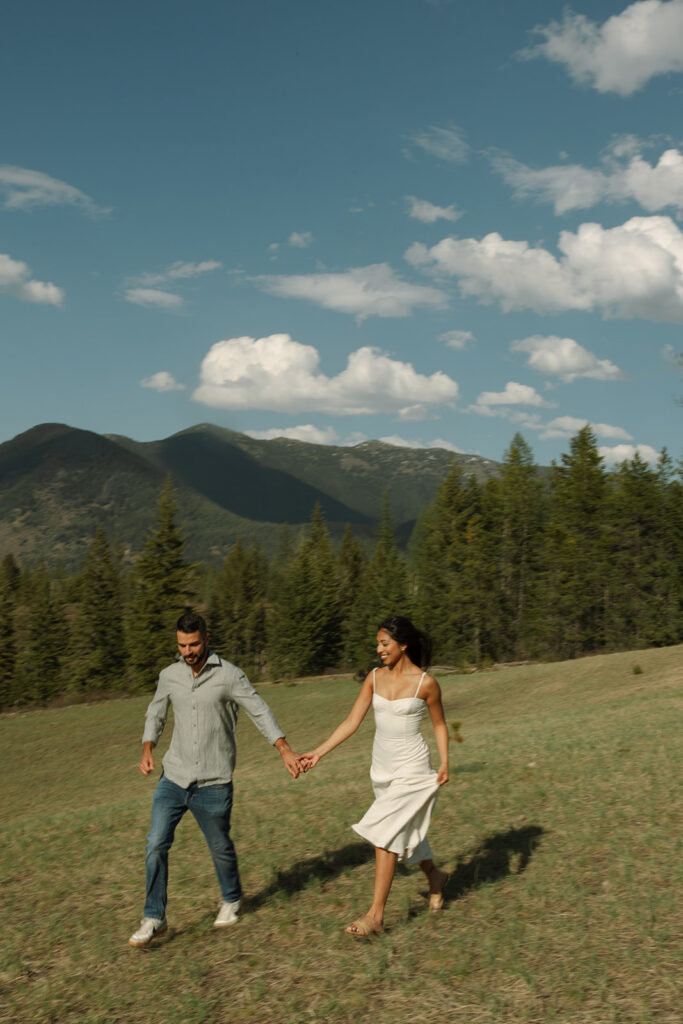 Candid engagement photo of couple exploring Glacier National Park with snowy peaks and spring landscape